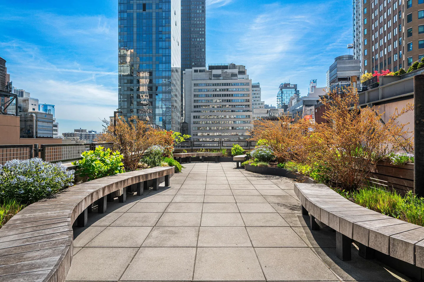 A rooftop garden with benches and plants under a blue sky.